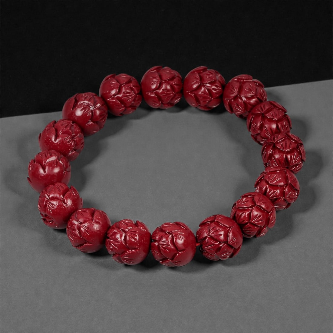 A Chinese Cinnabar Carved Bead Bracelet, 20th Century, 93FD: Composed of spherical beads carved from cinnabar, a mercury sulfide material traditionally used in Chinese ornamental objects. Each bead is centrally pierced and carved in moderate relief with stylize
