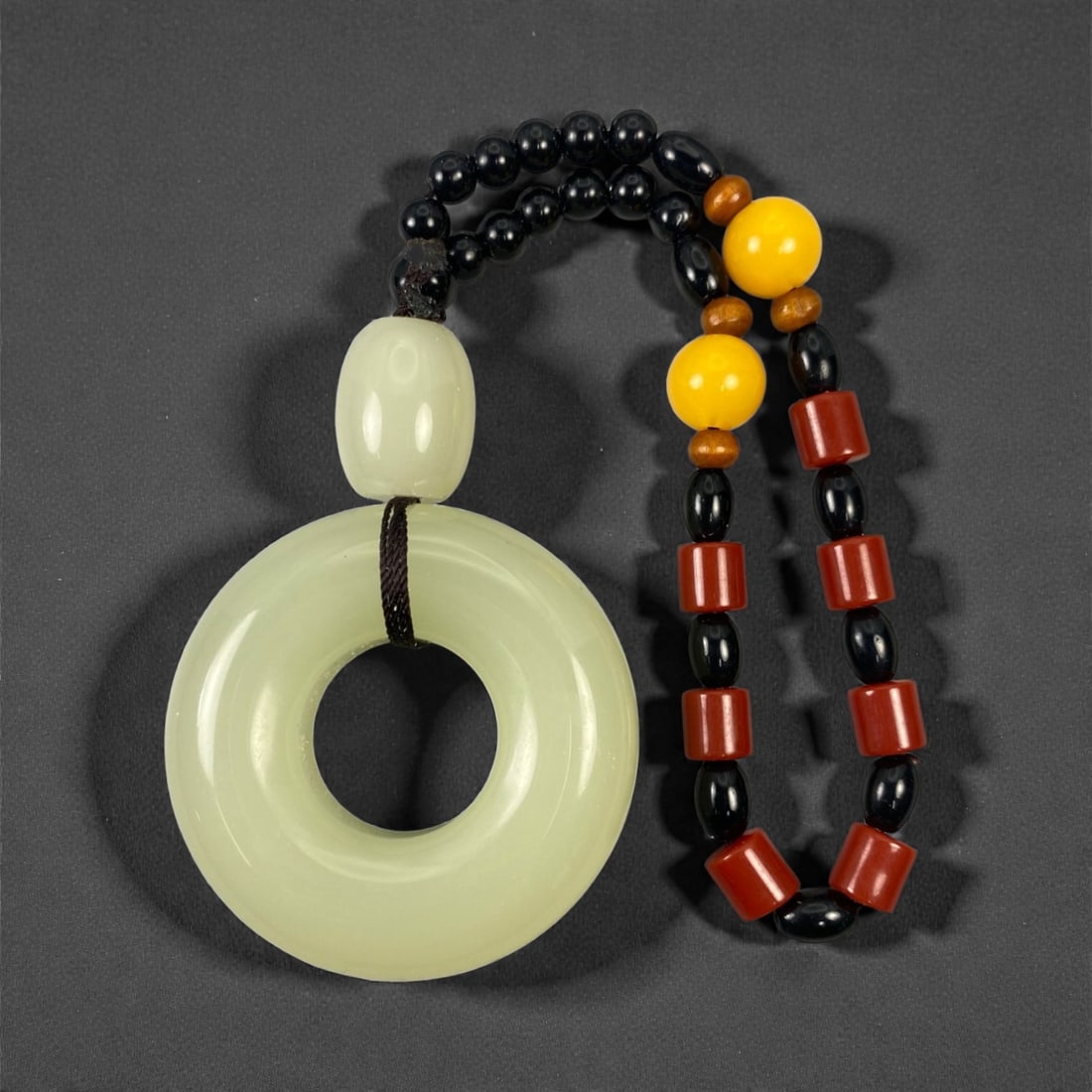 A Chinese Hetian Jade Bi Pendant with Beaded Necklace, 20th Century, 78FD: Carved from pale celadon-toned Hetian jade with a softly translucent body and an evenly polished surface. The pendant is formed as a thick circular disc with a central perforation, corresponding to th