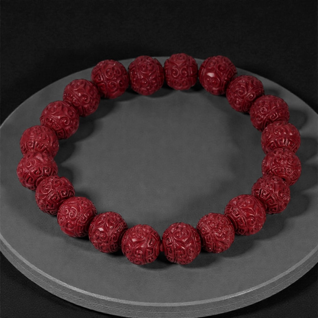 A Chinese Cinnabar Carved Bead Bracelet, 20th Century, 77YB: A Chinese cinnabar carved bead bracelet, 20th century. The bracelet is composed of uniformly carved spherical cinnabar beads, each finely decorated with dense scrolling and archaistic-style motifs cha