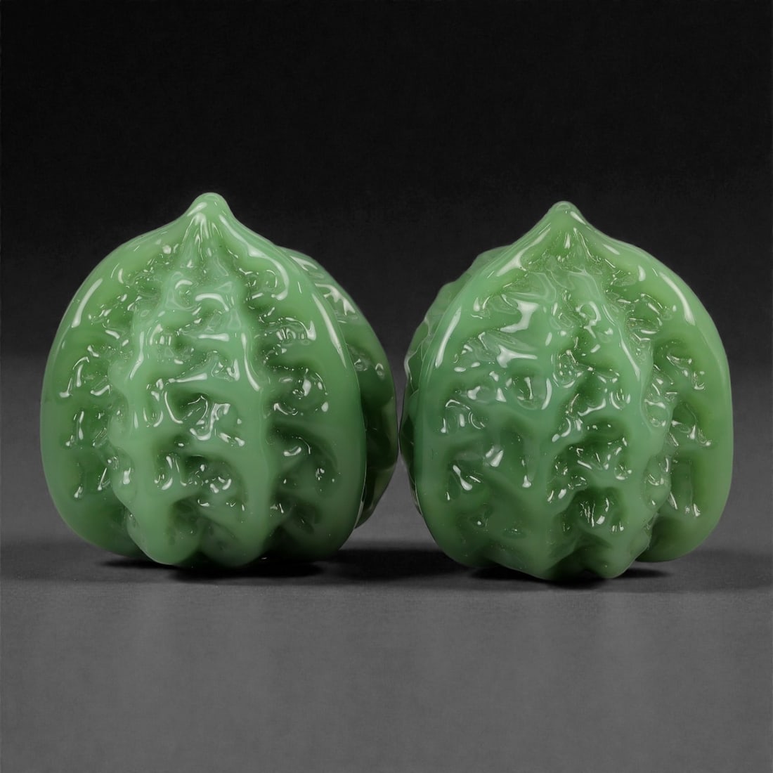 A Chinese Hetian Nephrite Jade Carved Walnut Pair, 20th Century, 76YB: Carved from green-toned Hetian nephrite with a semi-translucent body and a glossy polished surface, the matched pair is modeled in the form of "monkey head" walnuts (houtou hetao), with dense, rounded