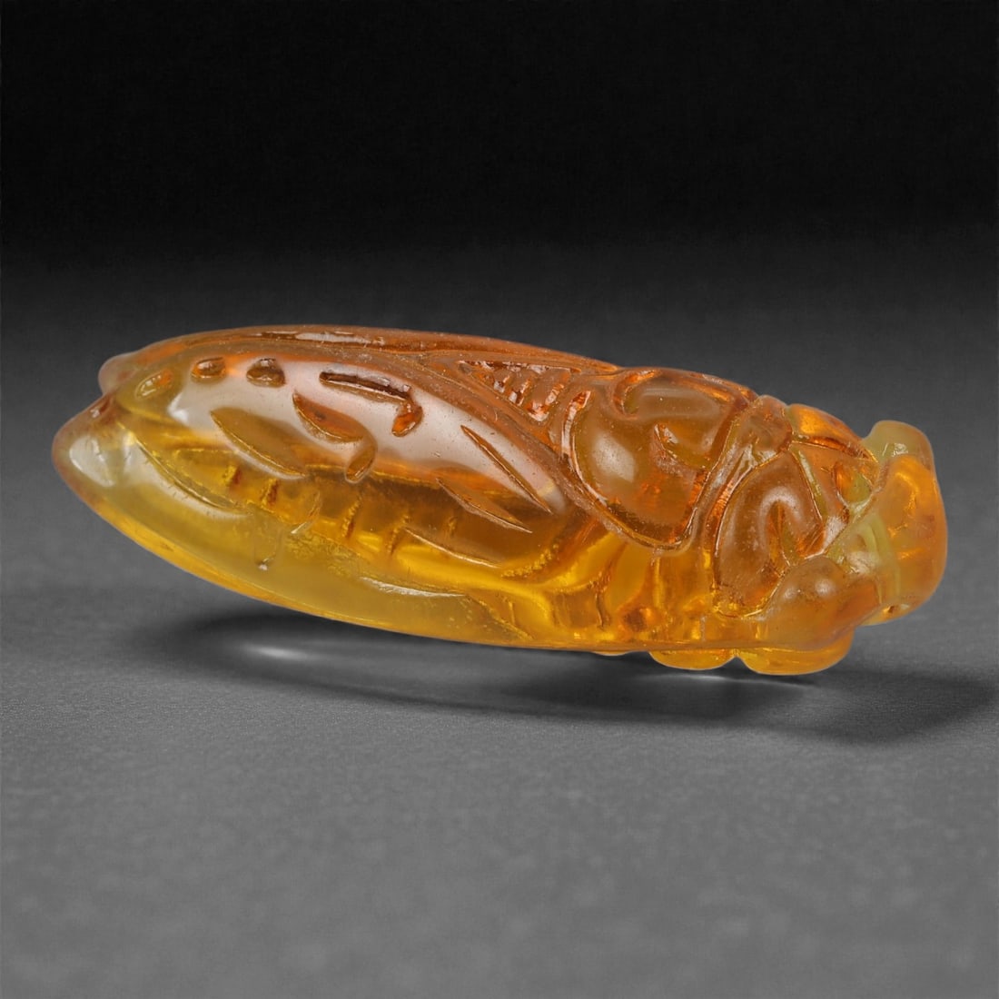 A Chinese Citrine Cicada Carving, 20th Century, 39YB: Carved from translucent citrine of warm golden-yellow tone with minor internal clouding, the figure represents a cicada shown in low relief with wings folded tightly along the elongated body, the head