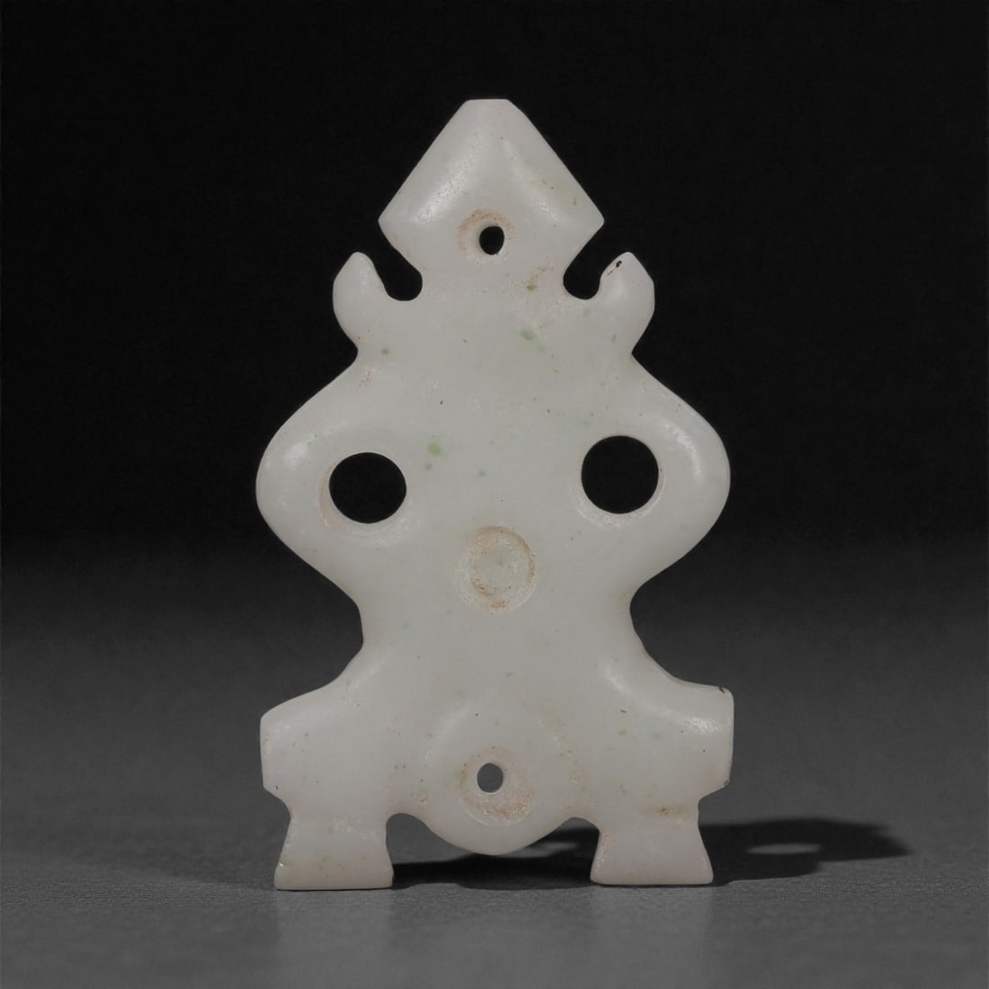 A Bactria-Margiana Marble Anthropomorphic Amulet, Late 3rd-2nd Millennium BCE, 40LP: Carved from white marble with minor pale inclusions, the amulet is shaped as a stylized anthropomorphic figure composed of a triangular head, flaring shoulders, and block-like legs. Three drilled perf