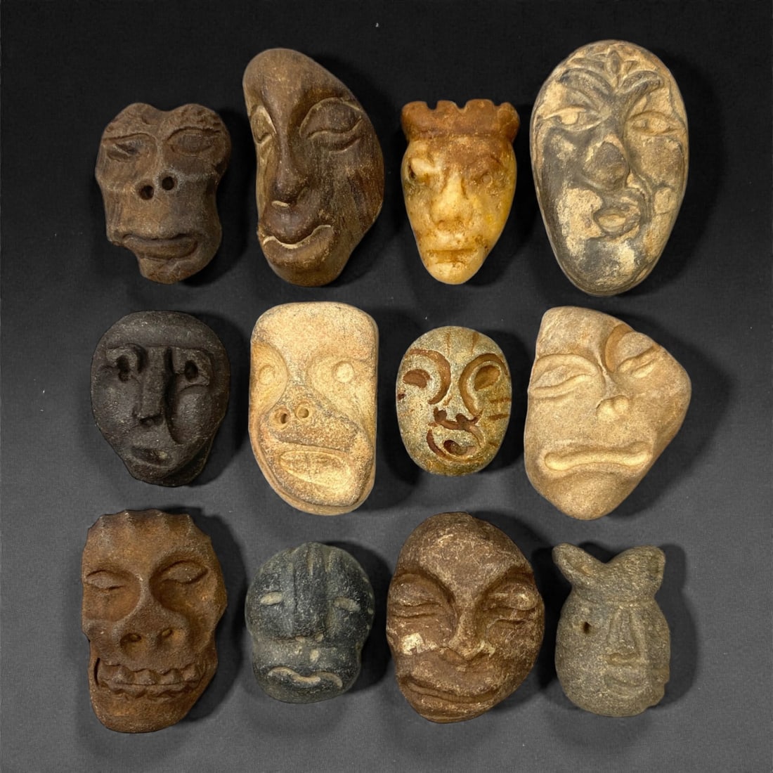 A Lot of Ancient Mediterranean Stone Maskettes, 12th-17th Century, 2.5-4.2cm, 34V: The group comprises lot of small maskettes carved from various stone types, including limestone and related sedimentary materials, displaying a range of natural tones from pale beige and ochre to dark