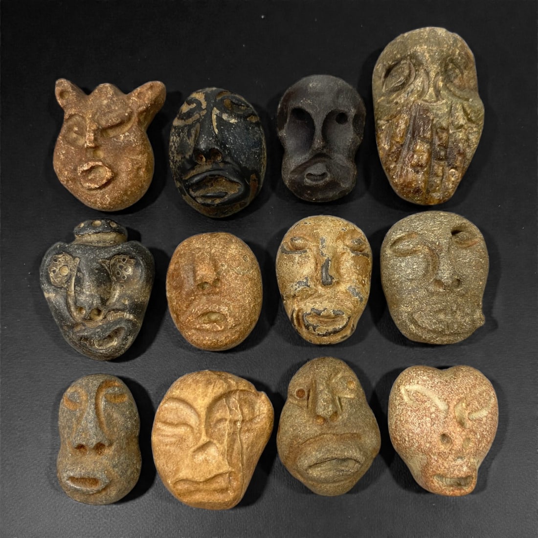 A Lot of Ancient Mediterranean Stone Maskettes, 12th-17th Century, 2.7-3.8cm, 36V: The group comprises lot of small maskettes carved from various stone types, including limestone and related sedimentary materials, displaying a range of natural tones from pale beige and ochre to dark