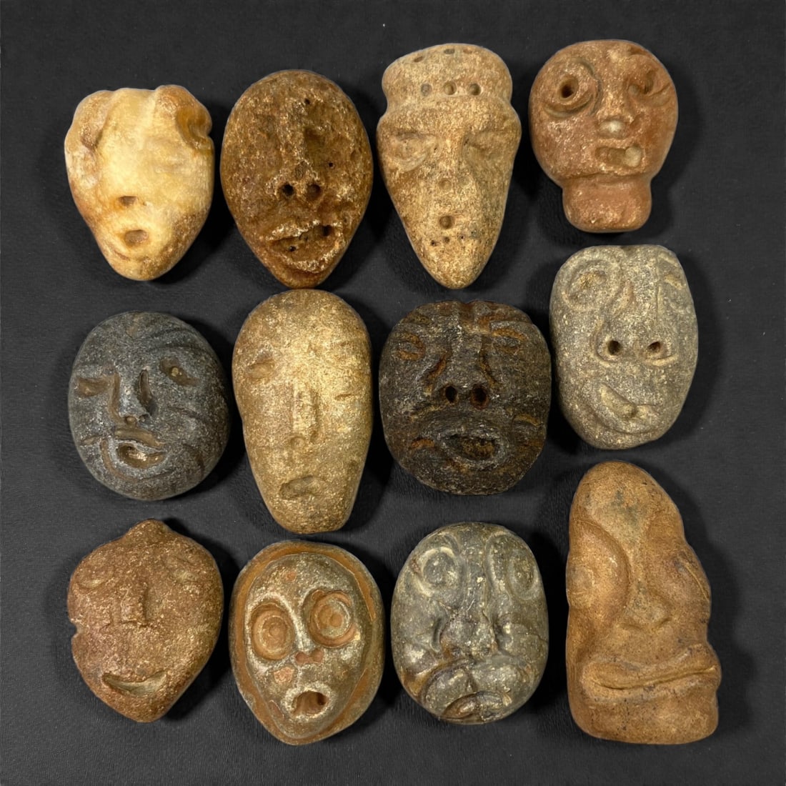 A Lot of Ancient Mediterranean Stone Maskettes, 12th-17th Century, 2.5-3.3cm, 47V: The group comprises lot of small maskettes carved from various stone types, including limestone and related sedimentary materials, displaying a range of natural tones from pale beige and ochre to dark