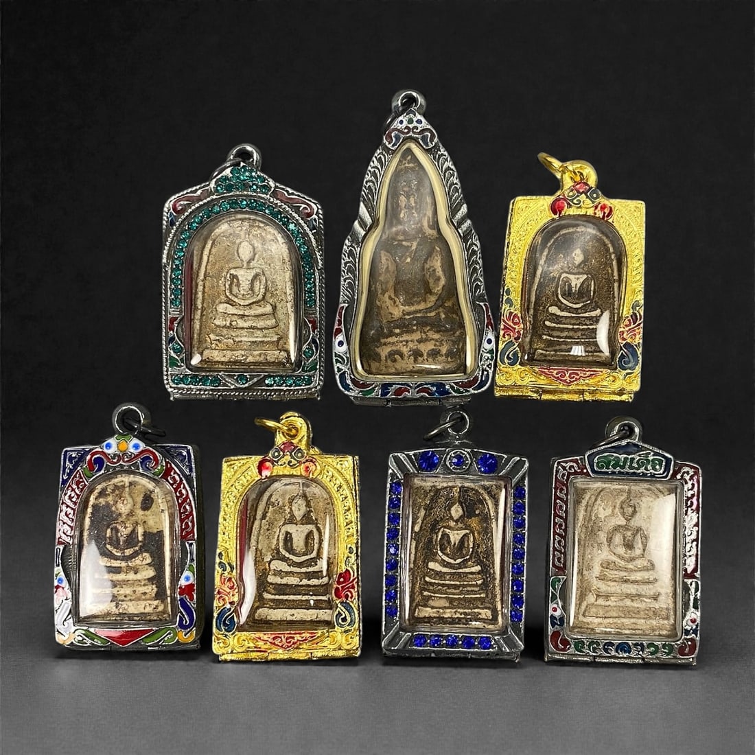 A Group of Seven Thai Buddhist Amulets, 20th Century, 23XJ: Comprising seven Thai Buddhist amulets formed from pale beige to buff and brown clay-based or composite materials, each molded in shallow relief and depicting a seated Buddha in meditation posture on 