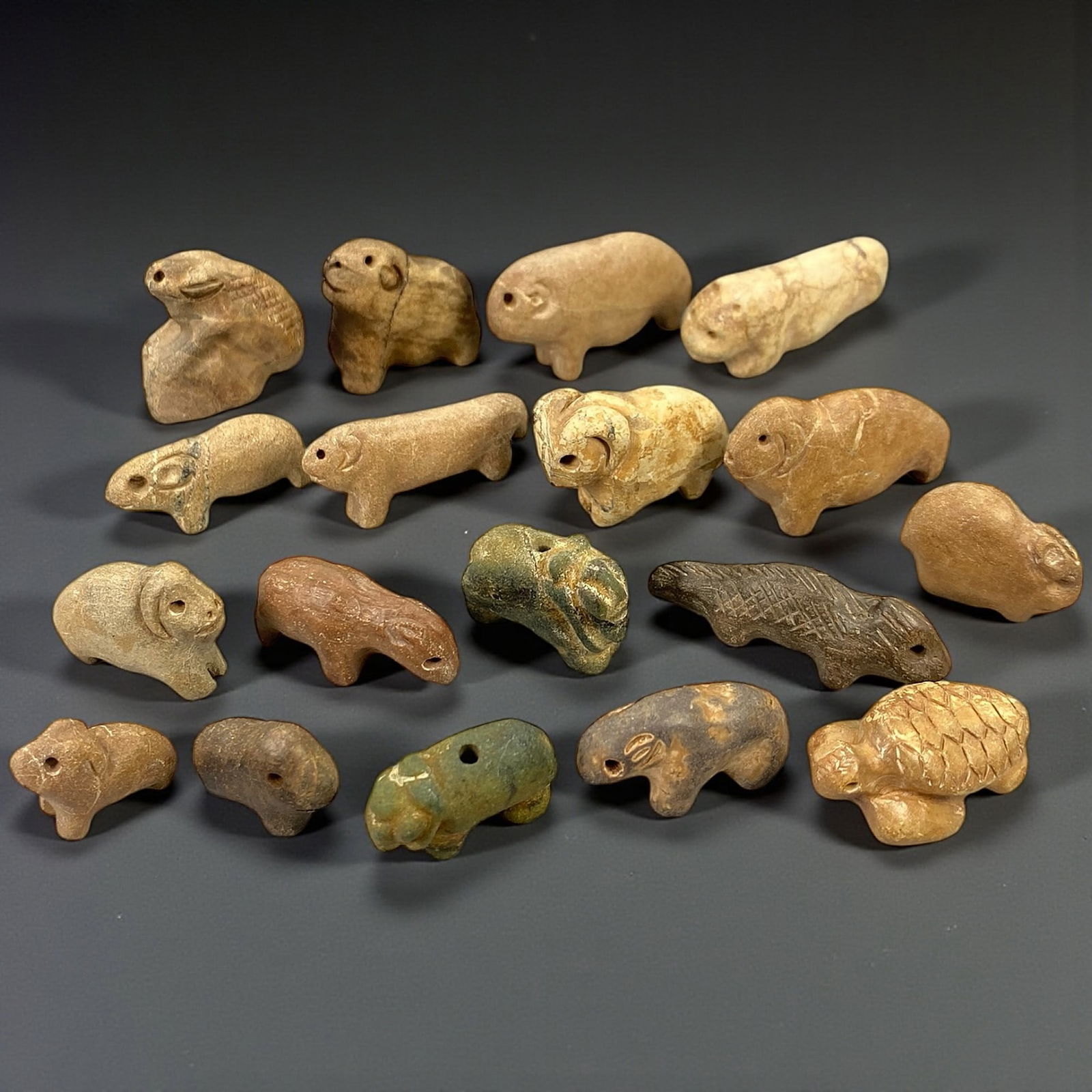 A Group of Near Eastern Stone Zoomorphic Figurines, 3rd-2nd Millennium BCE, 65V: Comprising eighteen small stone zoomorphic figurines carved in the round, representing stylized animals including quadrupeds and schematic creatures, worked from buff, brown, grey, and greenish stone