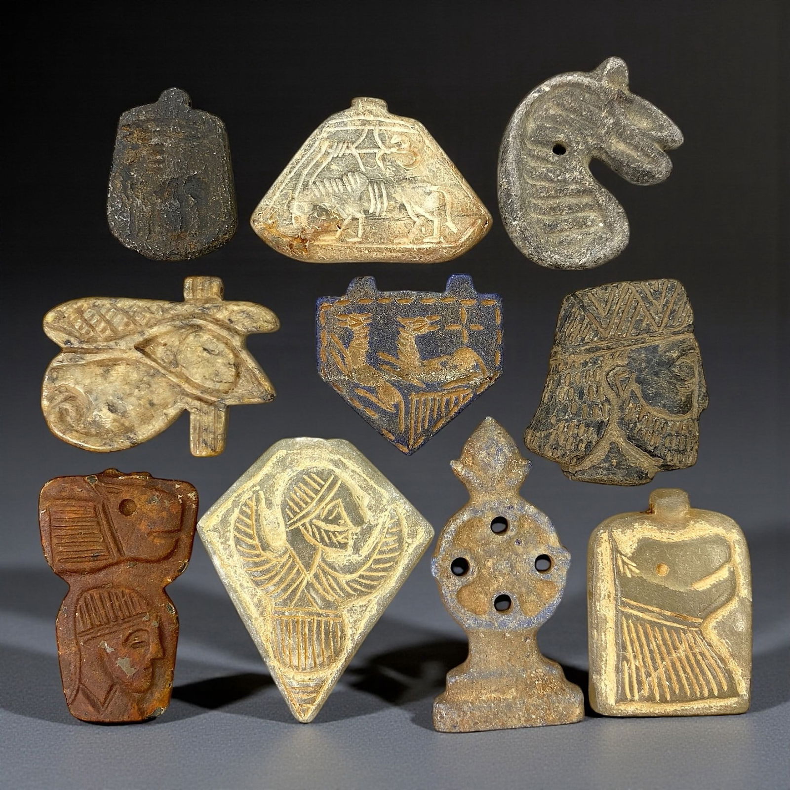 A Group of Ten Egyptian and Near Eastern Faience and Stone Amulets, Late Period, 57V: Comprising ten amulets carved or molded from faience, steatite, and related stone materials in tones ranging from pale beige and greenish buff to dark grey and brown, the group represents a range of p