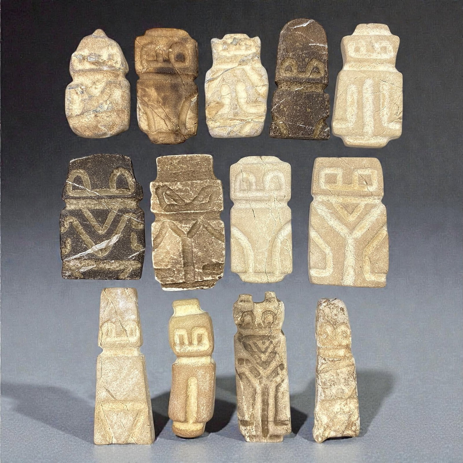 A Group of Valdivian Stone Anthropomorphic Figures, Circa 3500-1500 BCE, 72V: Comprising thirteen small anthropomorphic stone figures carved from light beige, grey, and brown stone, the group is rendered in a schematic and rectilinear style characteristic of Valdivian stone scu