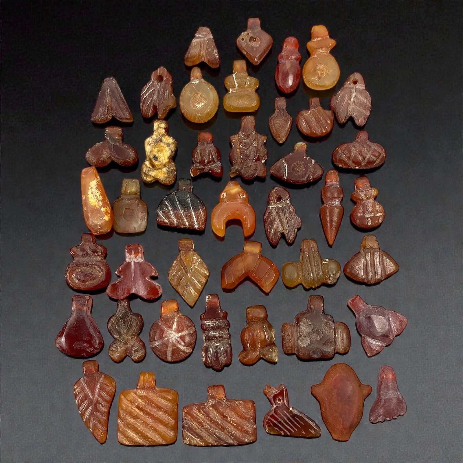A Group of Coptic Egyptian Carnelian Amulets, Late Antique Period, Circa 4th-7th Century CE, 95V: Comprising forty-three miniature amulets carved from carnelian, the group presents a dense assemblage of schematic symbolic and abstract forms, including foliate shapes, geometric pendants, stylized f