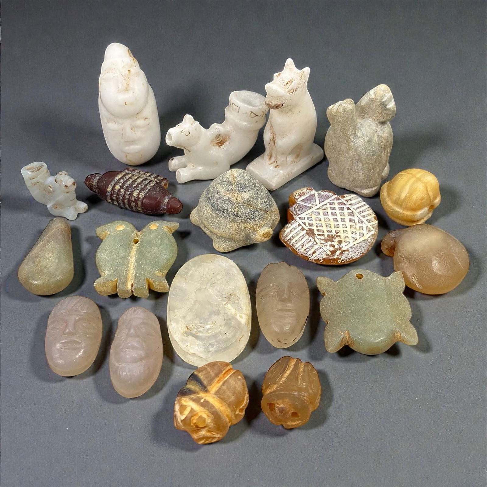 A Group of Ancient Stone and Hardstone Amulets and Miniature Figures, c. 1st Millennium BCE, 78V: Comprising nineteen small amulets and miniature figures carved from stone and hardstone materials of varying translucency and color, the group includes anthropomorphic heads, zoomorphic figures, turtl