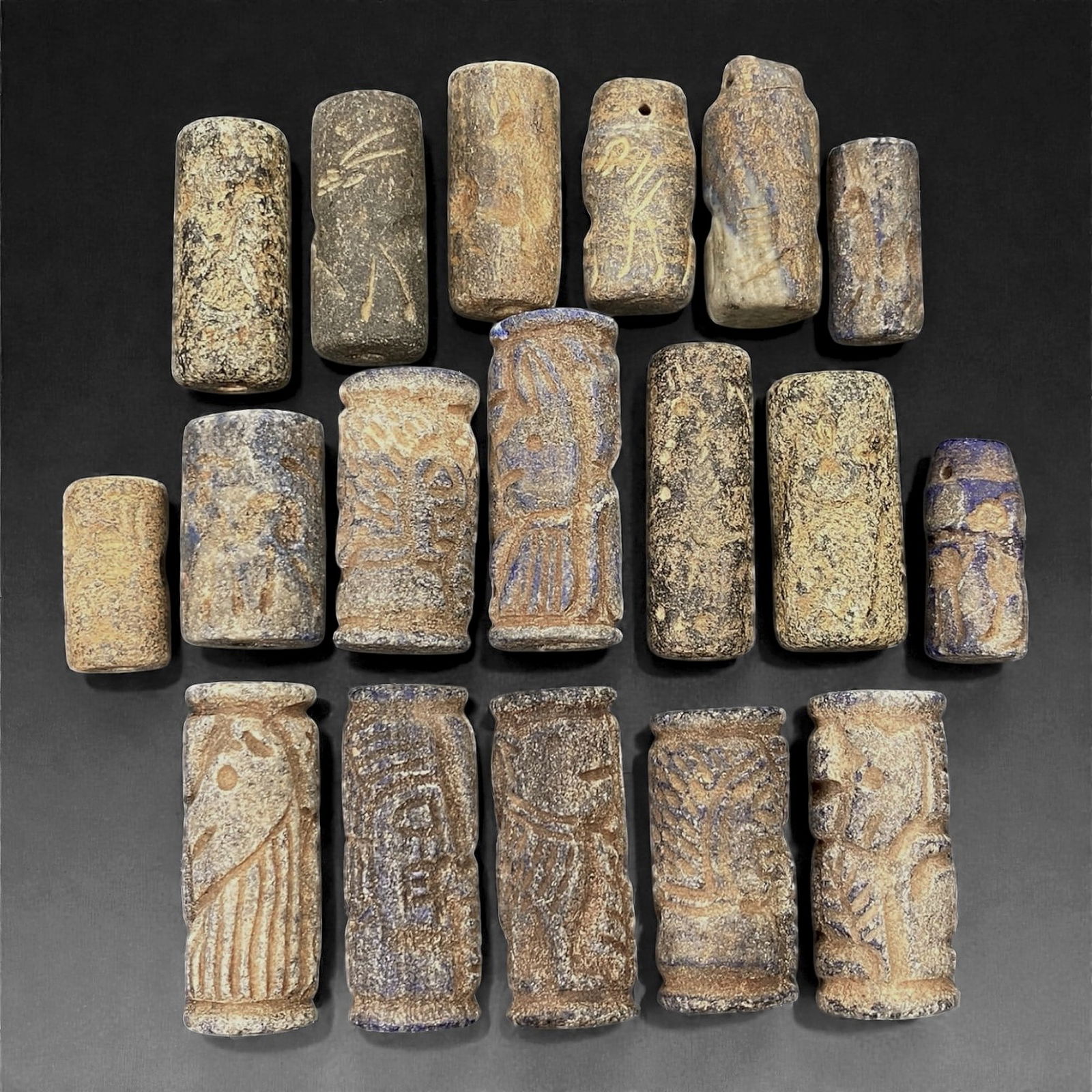 A Group of Near Eastern Lapis Lazuli Cylinder Seals, 2nd-1st Millennium BCE, 75V: Comprising eighteen cylinder seals carved from blue to grey-blue lapis lazuli, many with areas of calcite mottling and surface accretion consistent with age. The seals are cylindrical in form, with fl