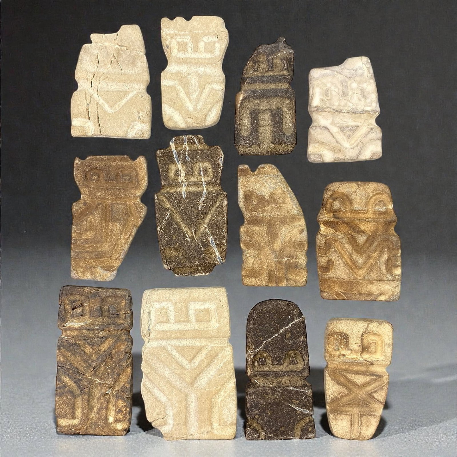 A Group of Valdivian Stone Anthropomorphic Figures, Circa 3500-1500 BCE, 74V: Comprising twelve small anthropomorphic figures carved from stone of varying tones, including pale beige, buff, and darker brown hues, each with visible granular texture and natural inclusions. The fi