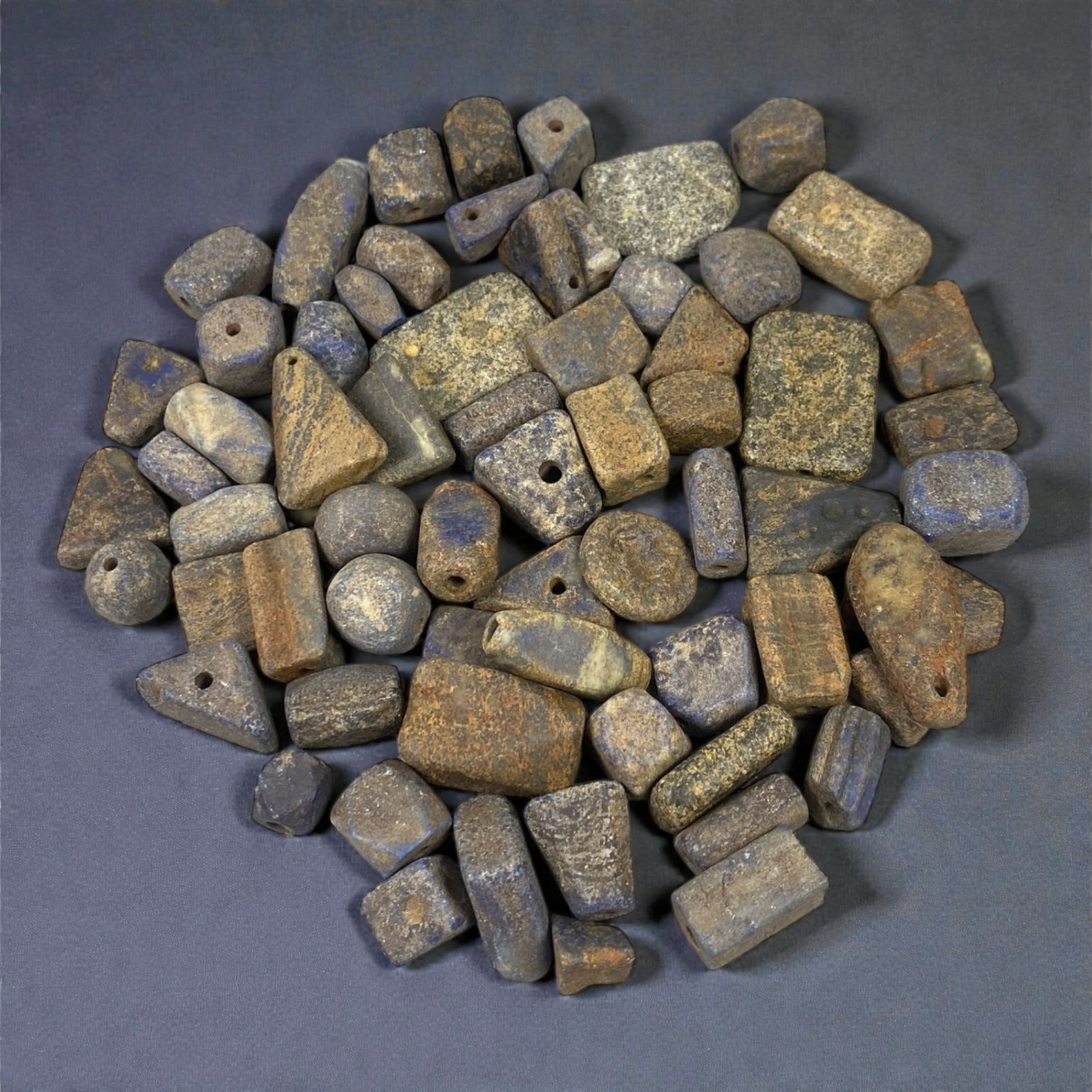 A Group of Mesopotamian Lapis Lazuli Beads, 3rd-2nd Millennium BCE, 32W: Comprising sixty-six beads carved from lapis lazuli of varied tonal quality, the group includes rectangular, barrel-shaped, cylindrical, discoid, and irregular geometric forms, each pierced longitudin