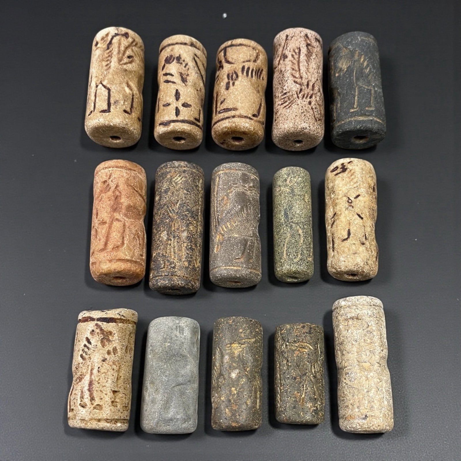 A Group of Near Eastern Stone Cylinder Seals, Mesopotamia, 3rd-2nd Millennium BCE, 42W: Comprising fifteen cylindrical seals carved from a range of stone materials, including buff, beige, grey, and dark stone with natural inclusions and surface variation. Several examples are engraved wi