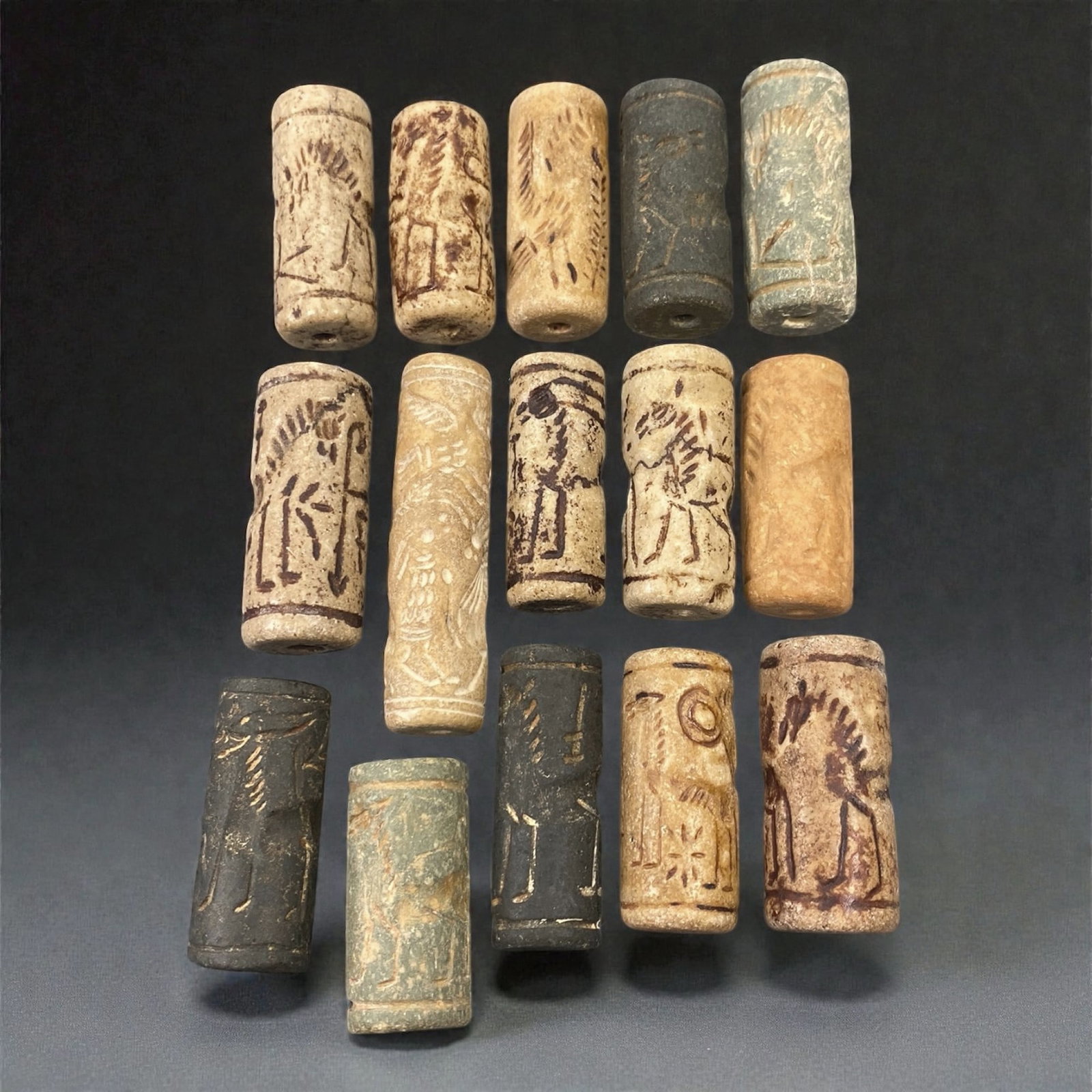 A Group of Near Eastern Stone Cylinder Seals, Mesopotamia, 3rd-2nd Millennium BCE, 41W: Comprising fifteen cylindrical seals carved from a range of stone materials, including buff, beige, grey, and dark stone with natural inclusions and surface variation. Several examples are engraved wi