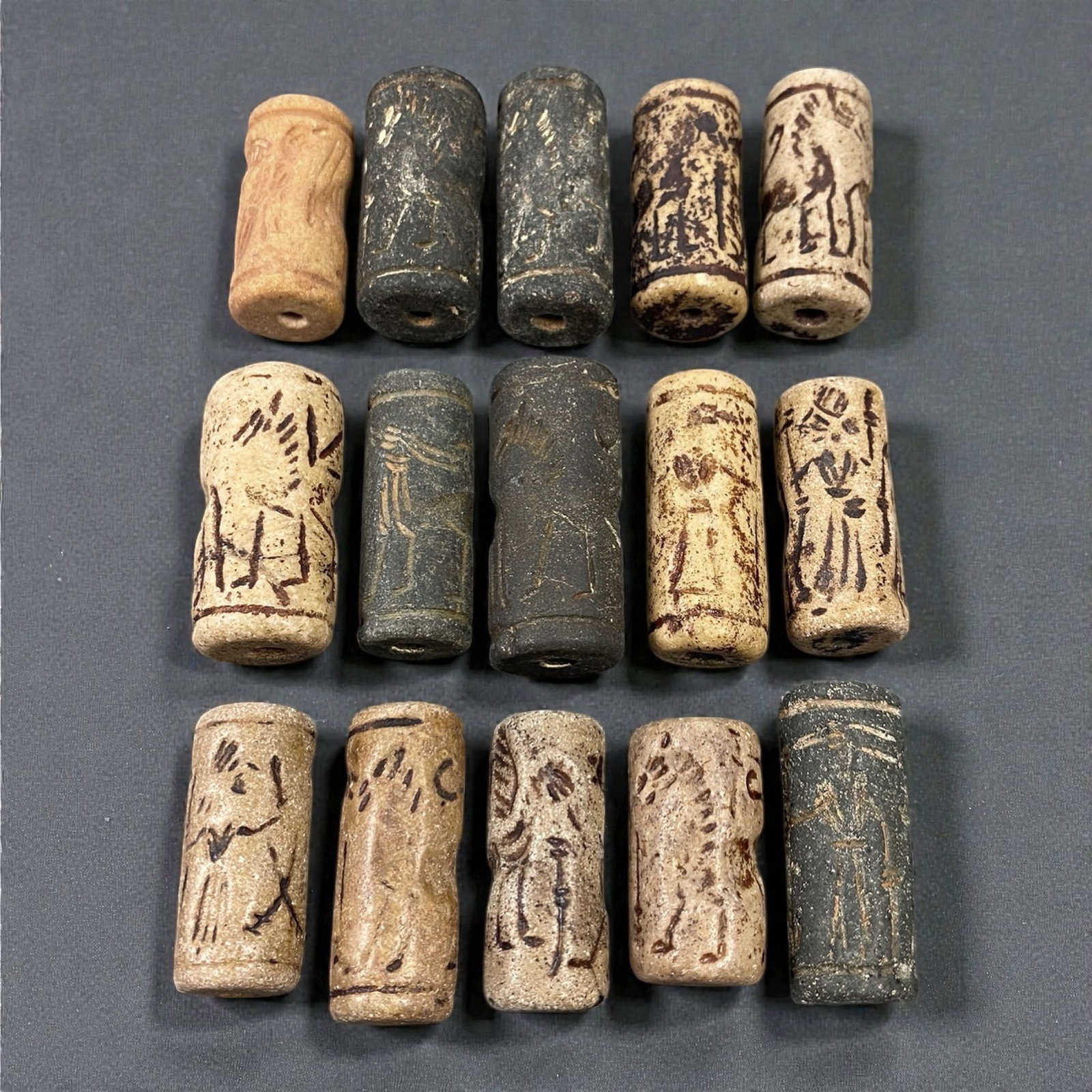 A Group of Near Eastern Stone Cylinder Seals, Mesopotamia, 3rd-2nd Millennium BCE, 47W: Comprising fifteen cylindrical seals carved from a range of stone materials, including buff, beige, grey, and dark stone with natural inclusions and surface variation. Several examples are engraved wi