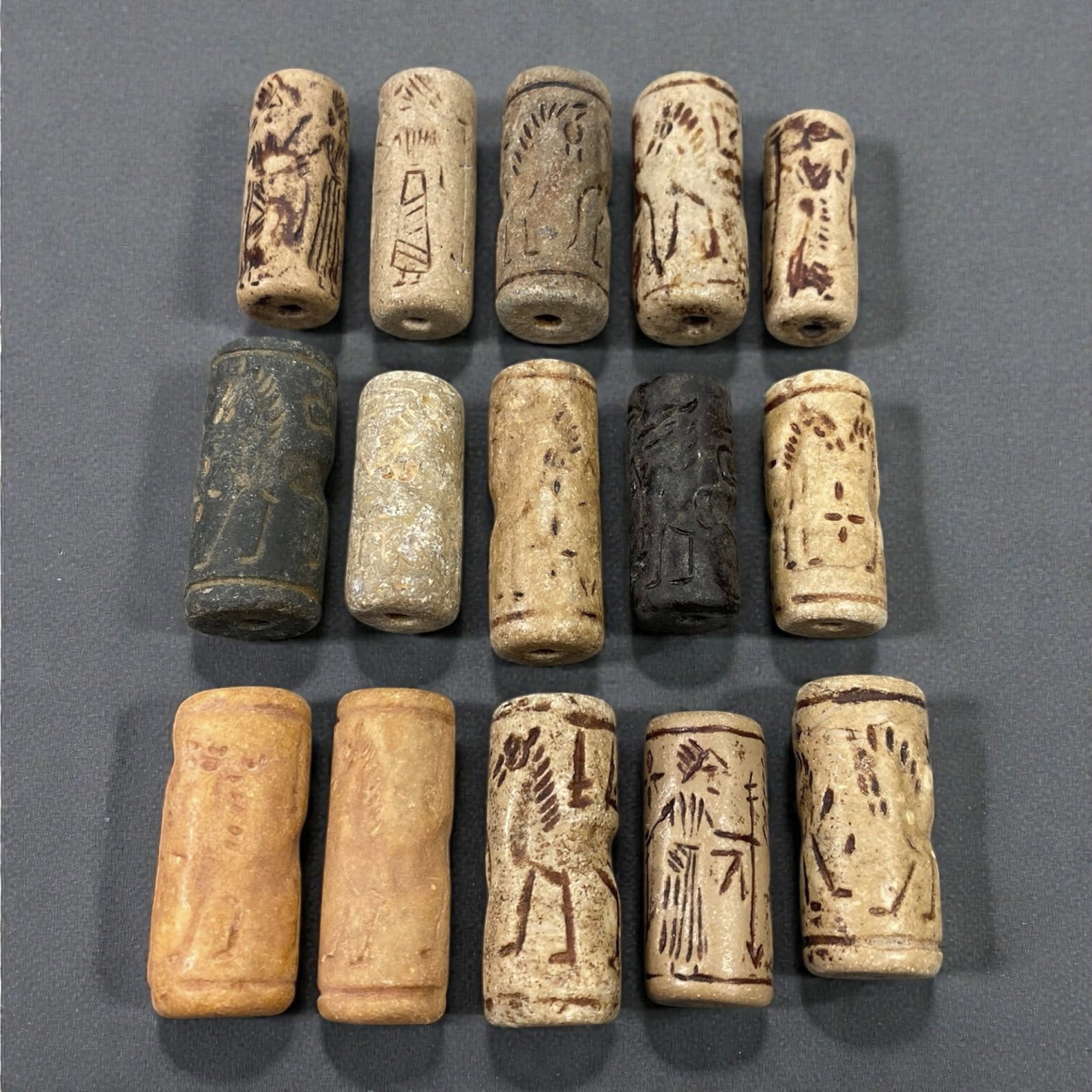 A Group of Near Eastern Stone Cylinder Seals, Mesopotamia, 3rd-2nd Millennium BCE, 43W: Comprising fifteen cylindrical seals carved from a range of stone materials, including buff, beige, grey, and dark stone with natural inclusions and surface variation. Several examples are engraved wi