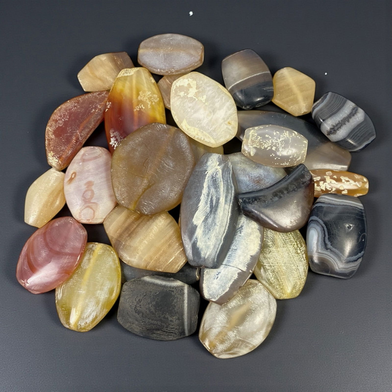 A Group of Persian Agate Beads, Parthian-Sasanian Period, Circa 1st Millennium CE, 17W: Comprising twenty-nine beads carved from banded and translucent agate, the group includes flattened oval, polygonal, and irregular rounded forms, each drilled longitudinally for suspension. The stones