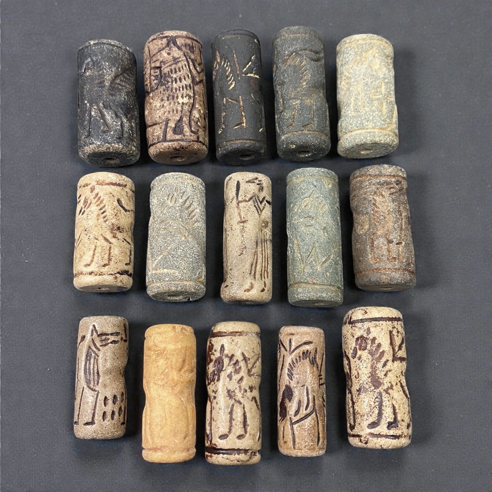 A Group of Near Eastern Stone Cylinder Seals, Mesopotamia, 3rd-2nd Millennium BCE, 40W: Comprising fifteen cylindrical seals carved from a range of stone materials, including buff, beige, grey, and dark stone with natural inclusions and surface variation. Several examples are engraved wi