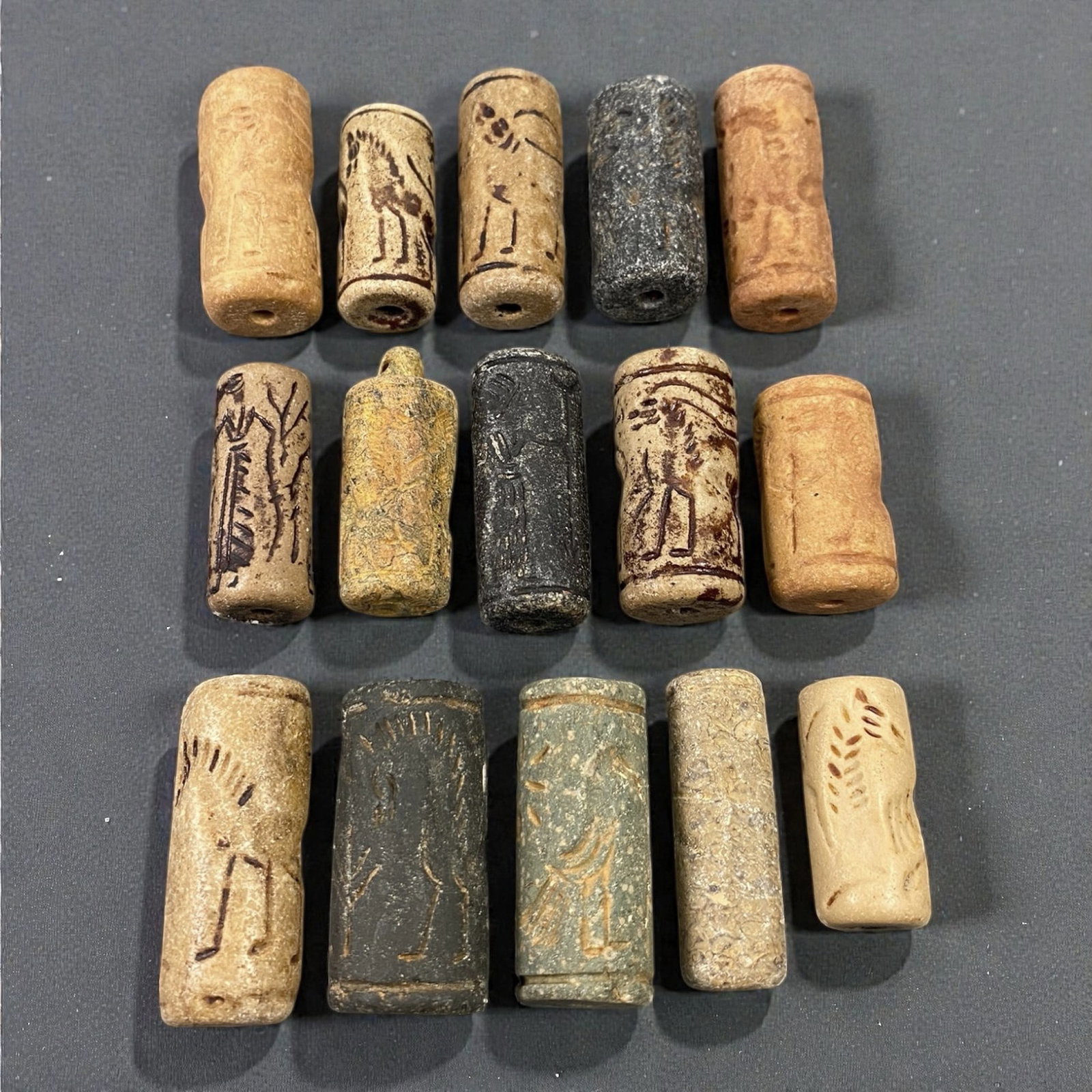 A Group of Near Eastern Stone Cylinder Seals, Mesopotamia, 3rd-2nd Millennium BCE, 38W: Comprising fifteen cylindrical seals carved from a range of stone materials, including buff, beige, grey, and dark stone with natural inclusions and surface variation. Several examples are engraved wi