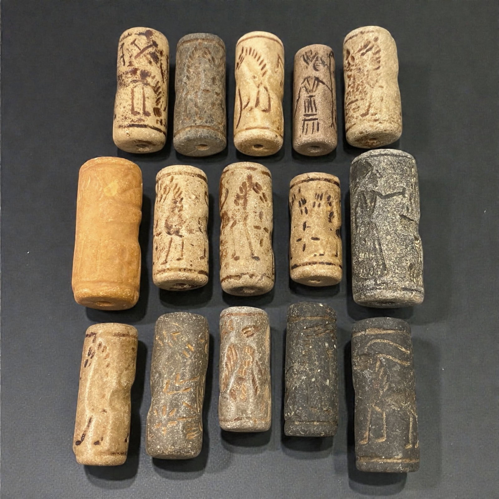 A Group of Near Eastern Stone Cylinder Seals, Mesopotamia, 3rd-2nd Millennium BCE, 44W: Comprising fifteen cylindrical seals carved from a range of stone materials, including buff, beige, grey, and dark stone with natural inclusions and surface variation. Several examples are engraved wi