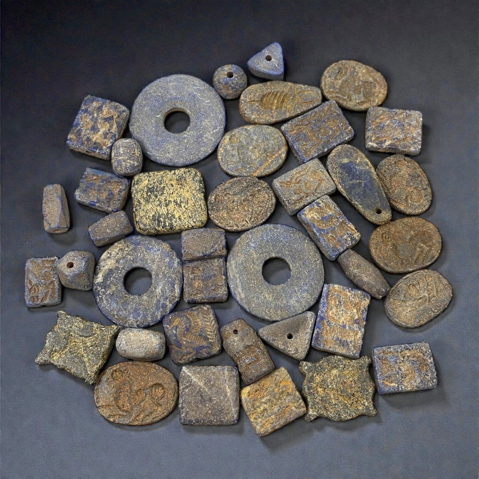 A Group of Mesopotamian Lapis Lazuli Beads, 3rd-2nd Millennium BCE, 30W: Comprising thirty-nine beads carved from lapis lazuli of varying tonal intensity, the group includes discoid, rectangular, cylindrical, triangular, and irregular geometric forms, several with central