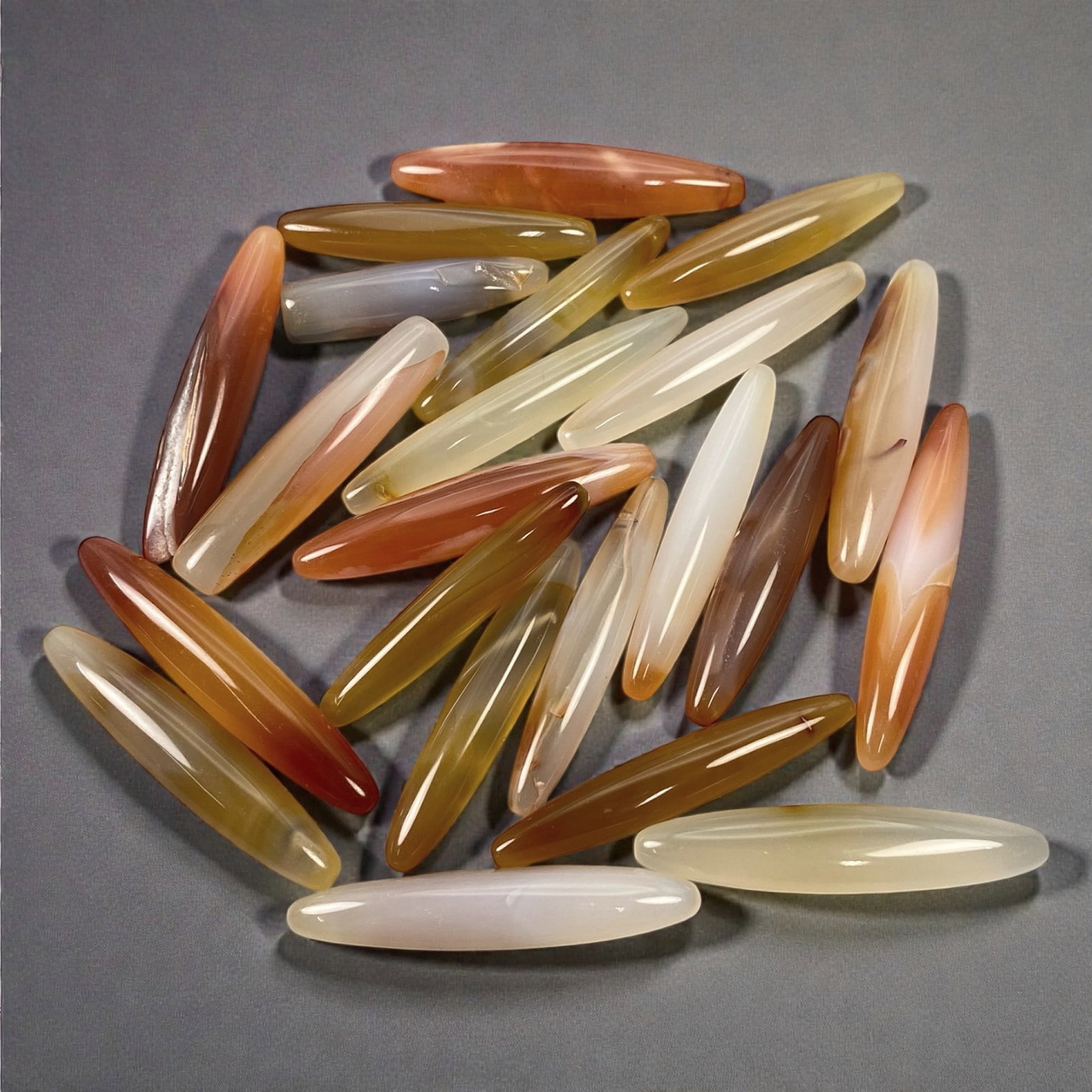 A Group of Tibetan Carnelian Ritual Beads, 19th-20th Century CE, 15W: The group comprises twenty-two elongated carnelian elements of tapering cylindrical and spindle-shaped form, carved from translucent chalcedony in tones ranging from pale cream and honey to orange, am