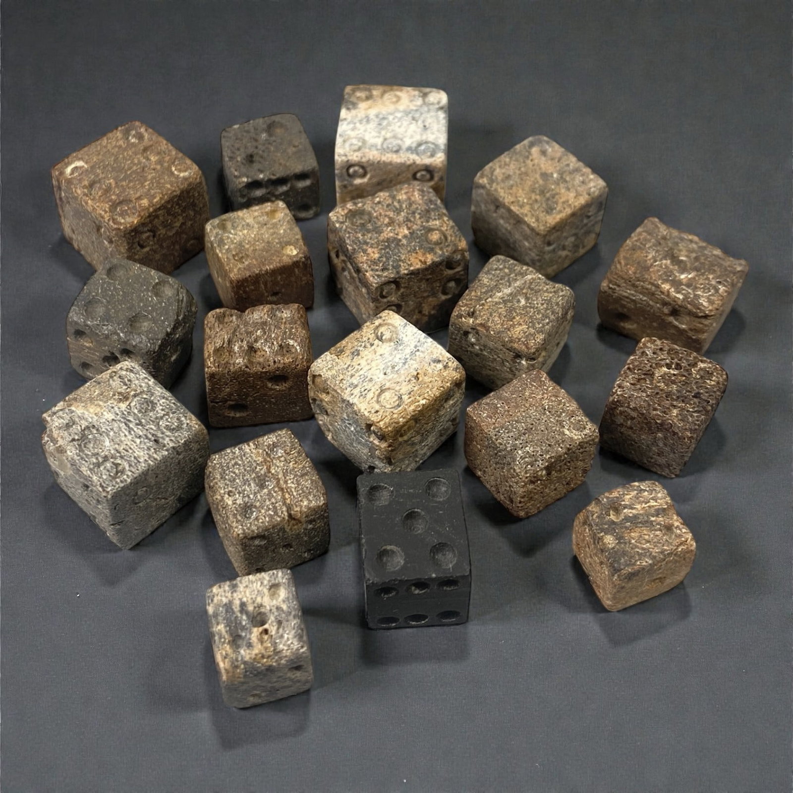 A Group of Roman Bone Dice, 1st-3rd Century CE, 34W: Comprising eighteen small cubic dice carved from bone, the group displays standard six-faced forms with recessed circular pips arranged according to Roman gaming conventions. The dice vary slightly in