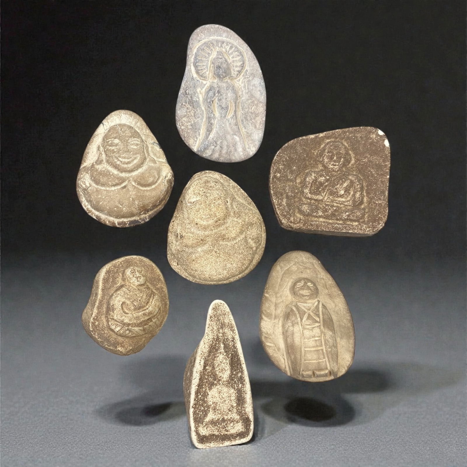 A Group of Japanese Stone Buddhist Figures, Edo Period, 57XJ: The group comprises seven small Buddhist devotional figures carved from grey and buff stone. The figures are rendered in low relief and shallow sculptural modeling, with softly rounded outlines and co