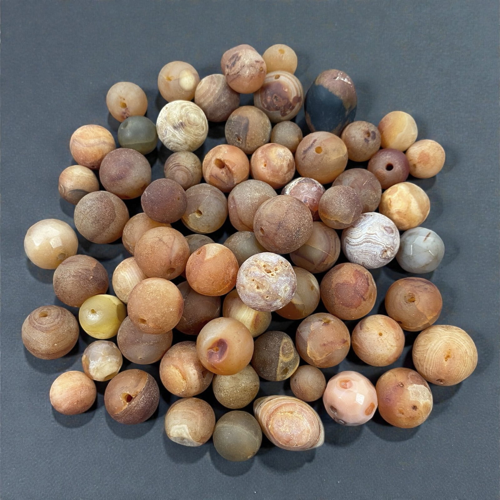A Tibetan Carnelian Bead Group, 18th-19th Century, 84W: Comprising seventy drilled carnelian beads of predominantly spherical and slightly irregular form, the group displays a broad range of warm tonal variation from pale cream and honey to orange, reddish
