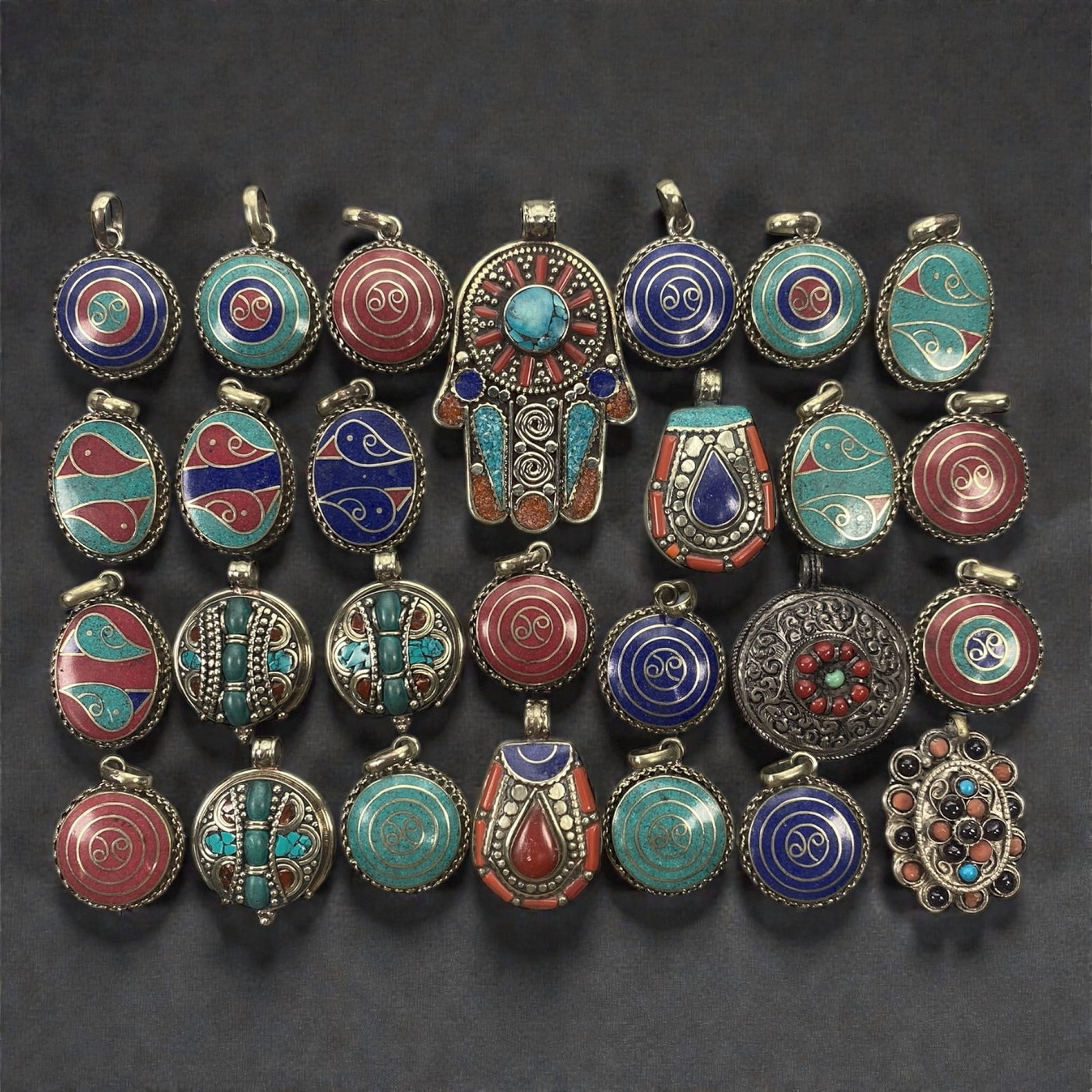 A Large Group of Silver and Enamel Amulets and Pendants, 20th Century, 67W: The group comprises twenty-seven silver-mounted amulets and pendants of varied size and form, including circular, oval, shield-shaped, and figural examples. The pieces are constructed primarily from s