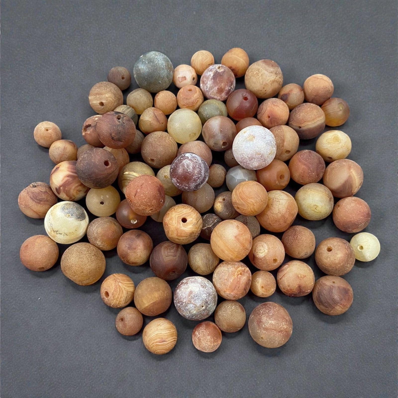 A Tibetan Carnelian Bead Group, 18th-19th Century, 86W: Comprising eighty-four drilled carnelian beads of predominantly spherical and slightly irregular form, the group exhibits a broad range of warm tonal variation from pale cream and honey to orange, red