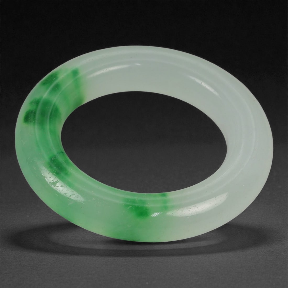 A Chinese Jadeite Jade Pendant, 20th Century, 52YB: Carved from translucent pale jadeite with concentrated bright green inclusions, worked as a circular ring pendant of uniform thickness. The form is defined by a rounded exterior edge and a smooth cent