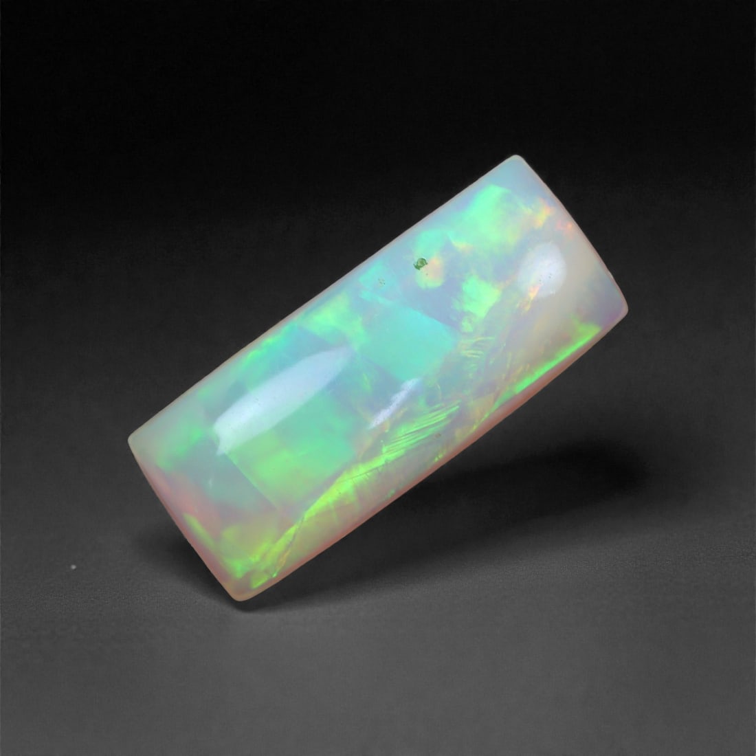 3.82 Carats Barrel-Cut Opal - Natural Ethiopian Stone 17.6x7.5x4.4mm, 43XH: This unique barrel-cut Welo opal dazzles with electric flashes of lime green, aqua, and fiery orange, all dancing through its elongated, cylindrical form. The stone's angular sides and rounded surface