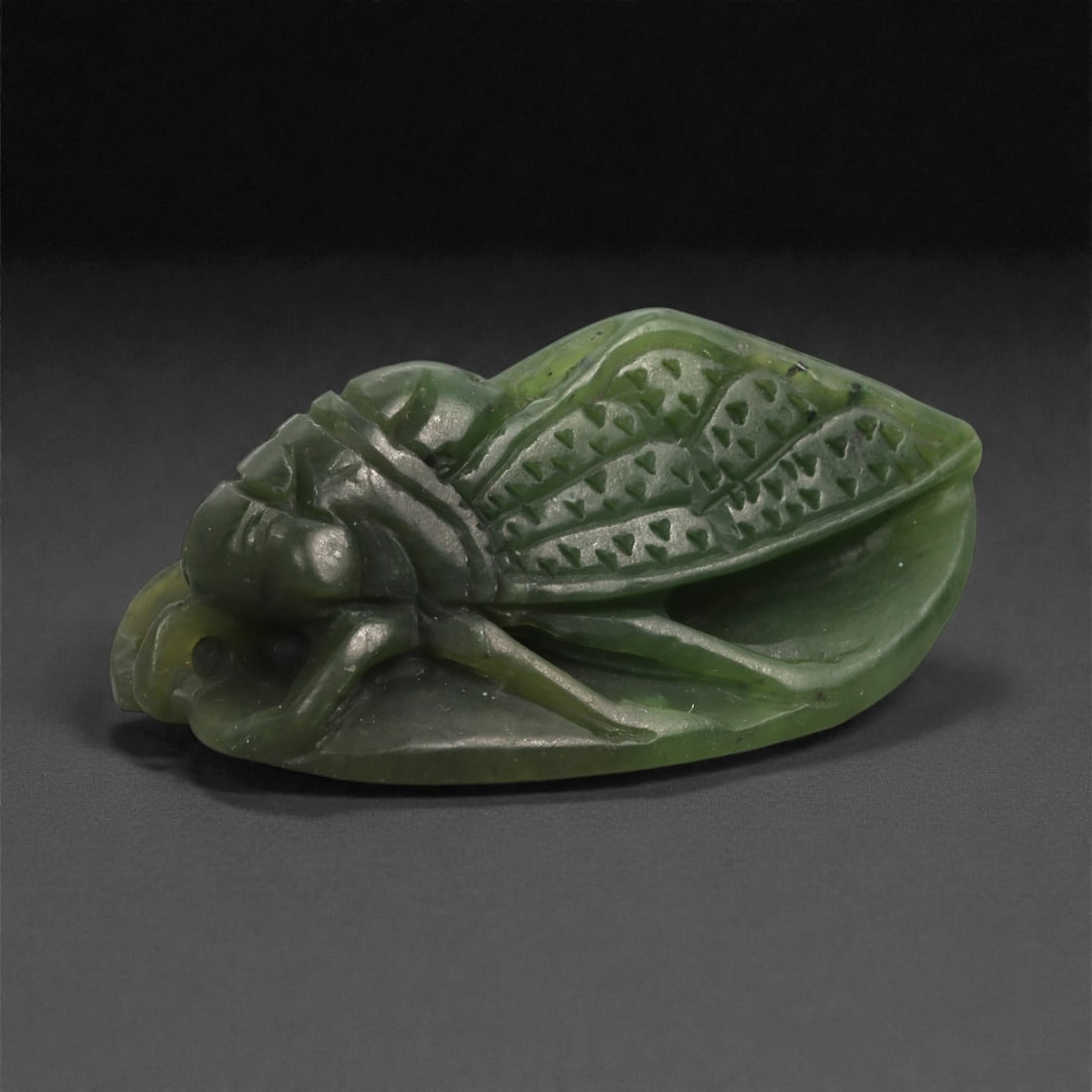 Chinese Dark Green Jade Cicada - Symbolic Amulet, 55ZD: Carved from rich dark green jade, this small sculptural amulet depicts a cicada rendered in stylized relief. The insect is shown resting with folded wings, carefully detailed with incised triangular m