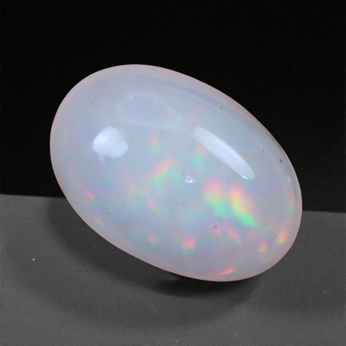 4.49 Carats Soft Fire Welo Opal - Natural Ethiopian Gemstone 13x9x6.5mm, 34XH: This Welo opal exudes a gentle, pastel fire that dances beneath its smooth, translucent surface. Flecks of neon green, peach, and lavender create a subtle mosaic of color, offering a delicate play-of-