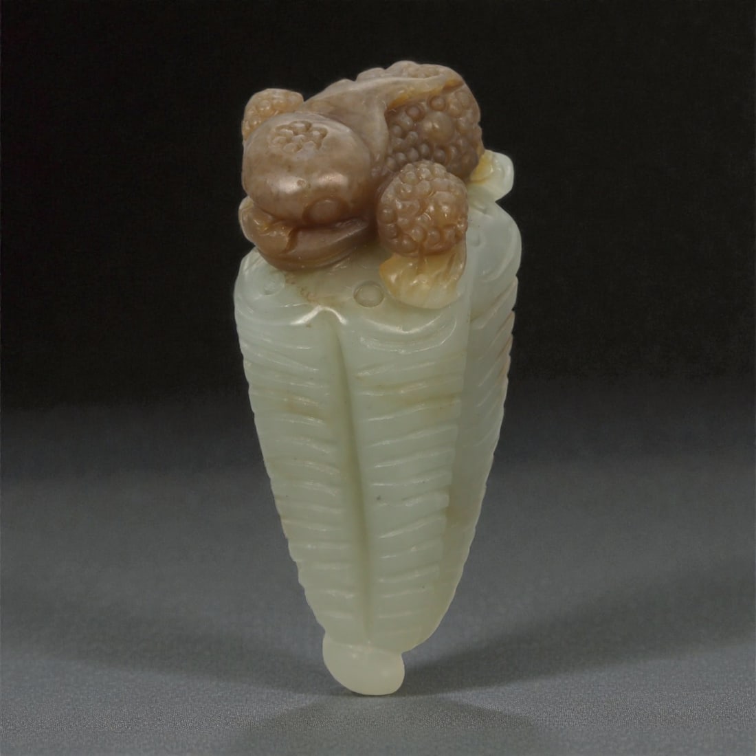 A Chinese Jadeite Pi Xiu Finial, 20th Century, 17FB: Carved from pale green jadeite with areas of russet-brown inclusions, the object is worked in the form of a pi xiu shown crouching atop an elongated, tapering element carved as a cicada. The pi xiu is