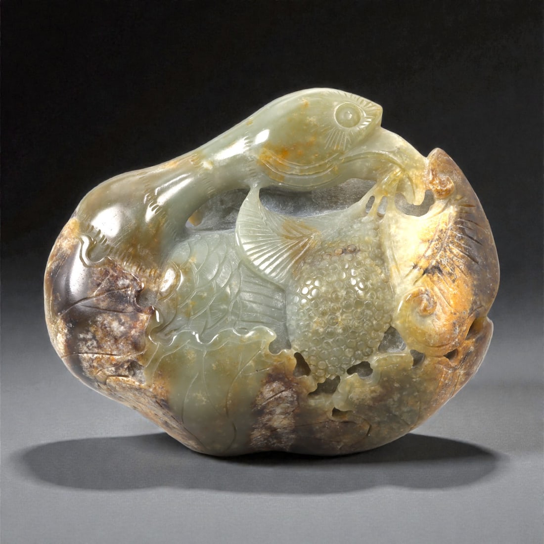 A Chinese Nephrite Jade Fish-Form Display Sculpture, 20th Century, 27FC: Carved from a large piece of Hetian nephrite jade with pale celadon tones interspersed with areas of russet and brown inclusions, the sculpture is worked as a freestanding display piece of rounded, ir