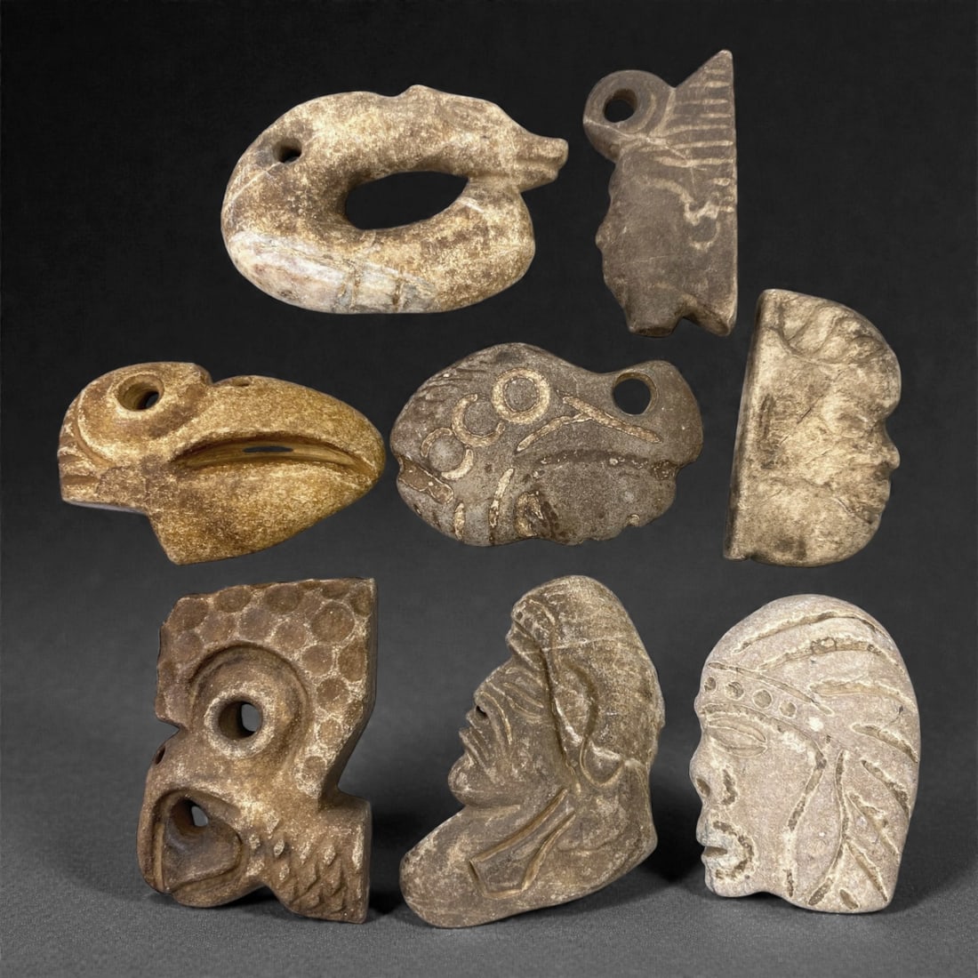 A Group of Mesoamerican Stone Sculptural Pendants, Pre-Columbian Period, 75XJ: Comprising eight stone pendants carved from light to dark-toned stone, the group includes stylized zoomorphic and anthropomorphic forms rendered in relief and partial three-dimensional modeling. Sever