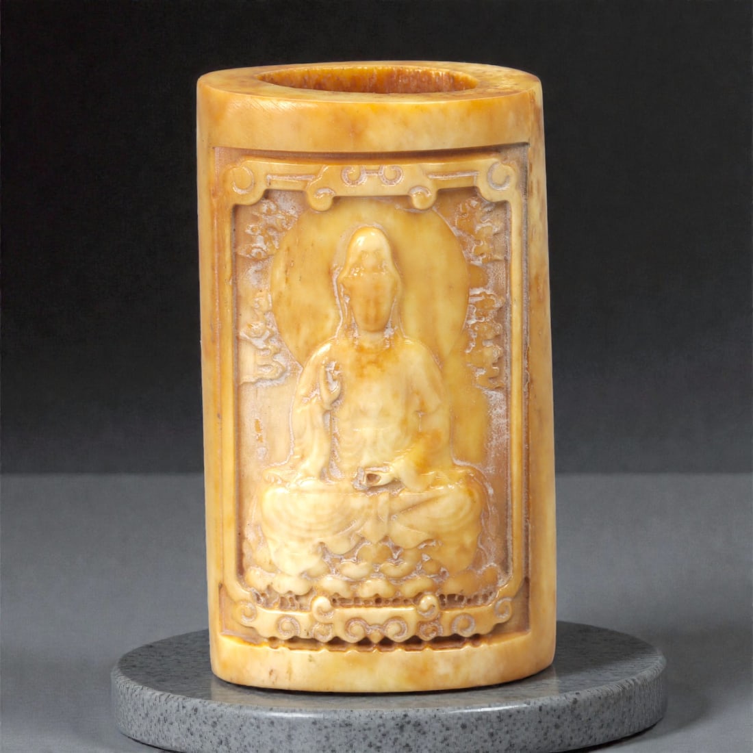 A Chinese Bone Carved Buddhist Figure Brush Holder, 20th Century, 36FC: Carved from pale yellow bone with natural translucency, tonal variation, and visible organic striations, the object is formed as a cylindrical sleeve with an open rim and an entirely open base. The in