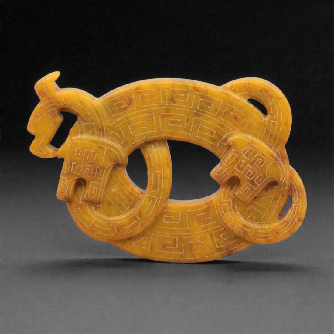 A Chinese Jade Openwork Plaque, Ancient Style, 20th Century, 39YC: The plaque is carved from jade of warm yellow-brown tone with areas of lighter translucency and natural mottling. It is worked as an openwork composition with a horizontally oriented form, incorporati