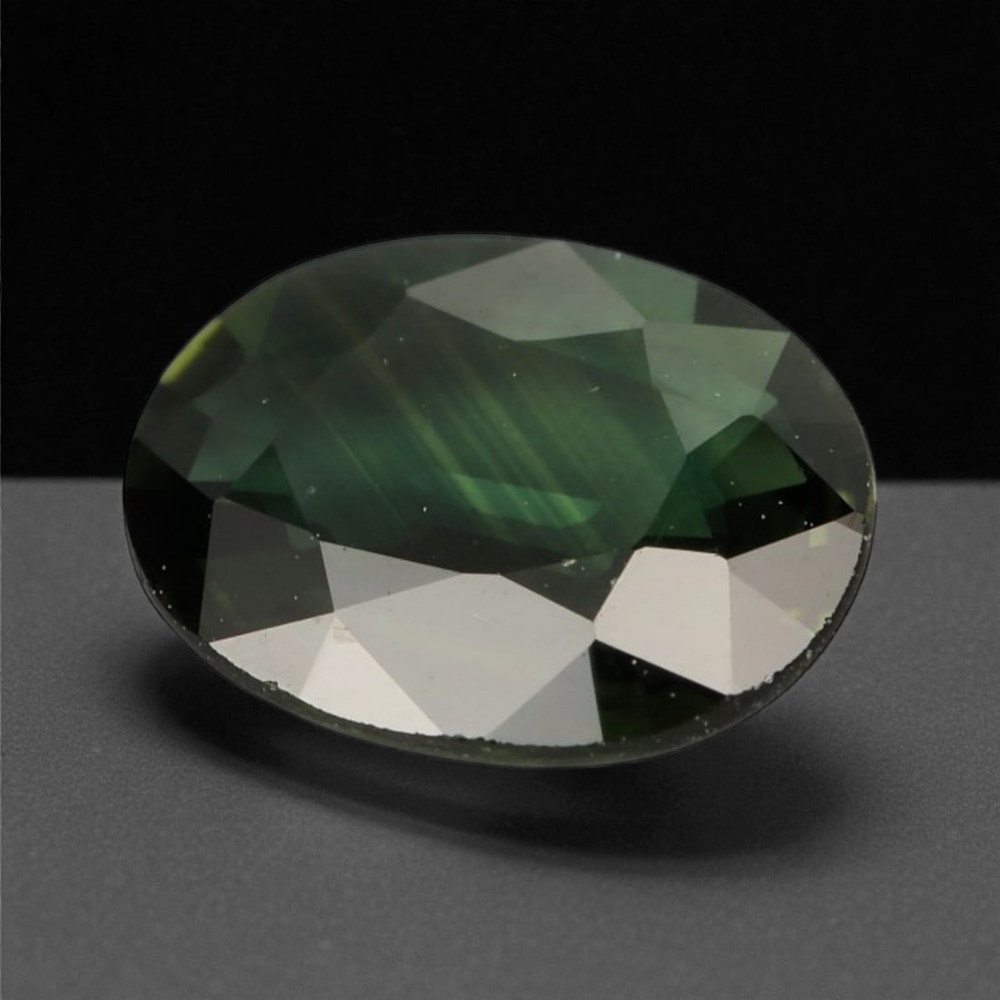 1.57 Carats Deep Green Sapphire - Natural Sri Lankan Stone - 8.6 x 6.9 x 2.7 mm, 81WE: This richly saturated sapphire exhibits a captivating forest green hue, enhanced by deep internal reflections and subtle silky zoning that lend depth and intrigue to its faceted oval shape. The surfac