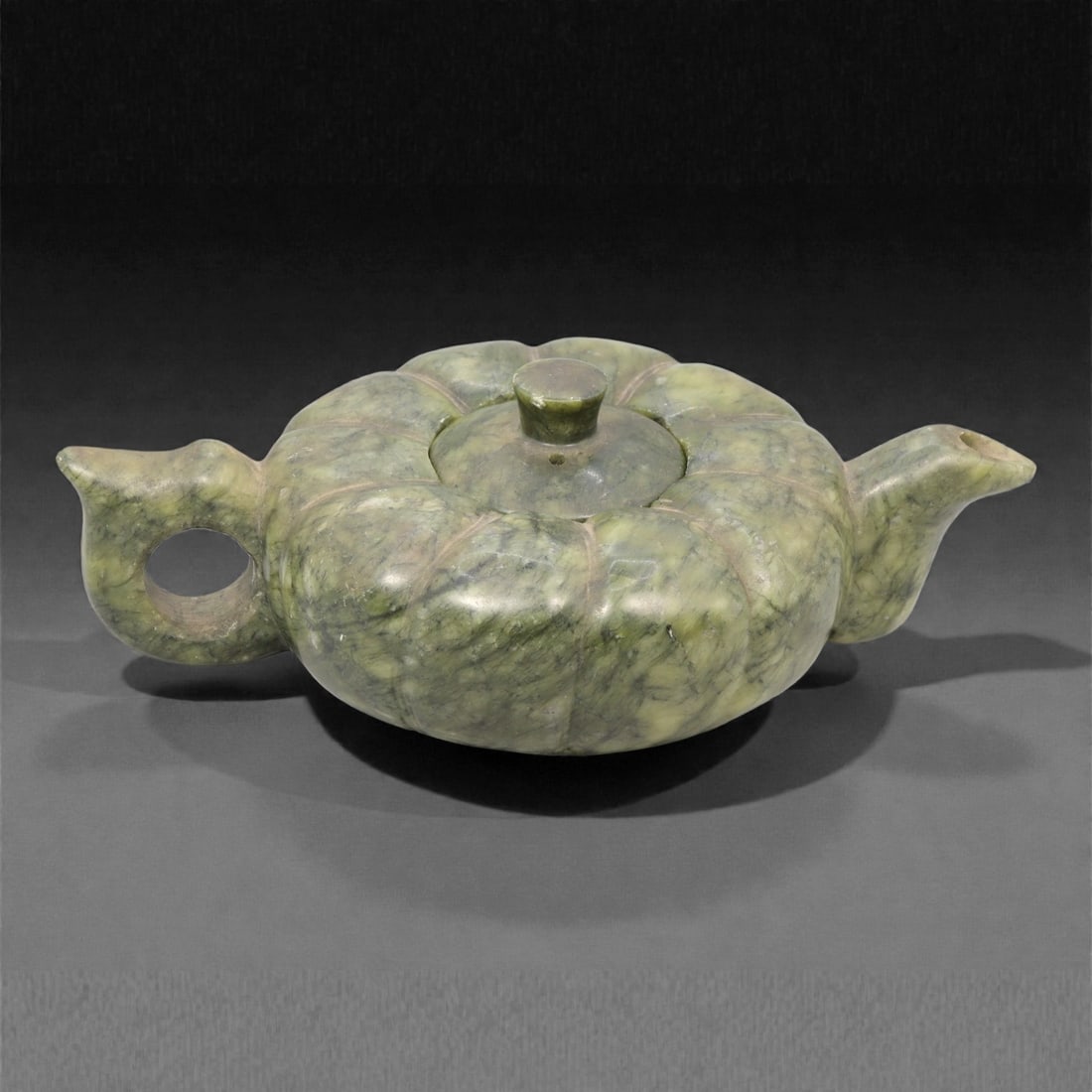 A Chinese Hetian Jade Teapot, 20th Century, 50YC: Carved from mottled green Hetian jade with cloudy translucency and darker mineral inclusions, the teapot is formed with a low, compressed lobed body divided into rounded segments radiating from the ce