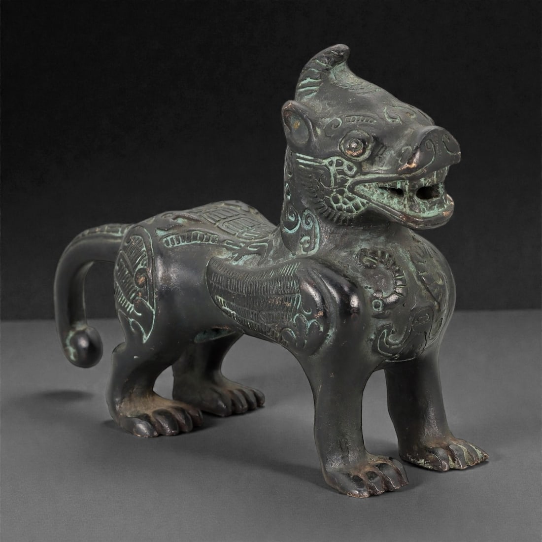 A Chinese Bronze Mythical Beast (Qilin/Bixie) Figure, 20th Century, 21FH: Cast in bronze and modeled as a striding mythical beast, the figure stands on four sturdy legs with the head raised and mouth open, revealing a hollow interior. The creature combines leonine and drago