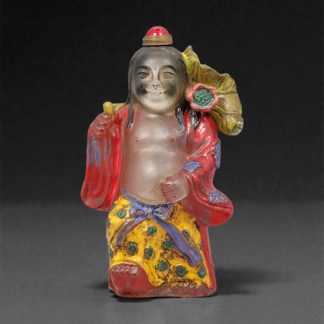 A Chinese Glass Figural Snuff Bottle, 20th Century, 61YC: Molded from translucent and opaque glass with applied polychrome coloration, the snuff bottle is formed as a standing male figure with a rounded torso and smiling facial expression. The figure is show