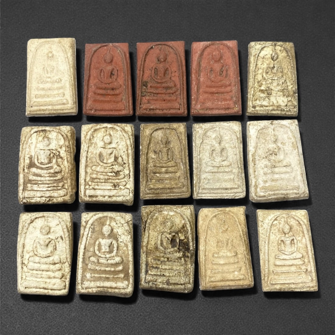 A Group of Thai Clay Buddhist Amulets, 20th Century, 79FK: The group comprises fifteen small rectangular clay amulets, each molded in low relief with a seated Buddha shown in meditation posture beneath an arched niche and raised on tiered bases. The amulets a