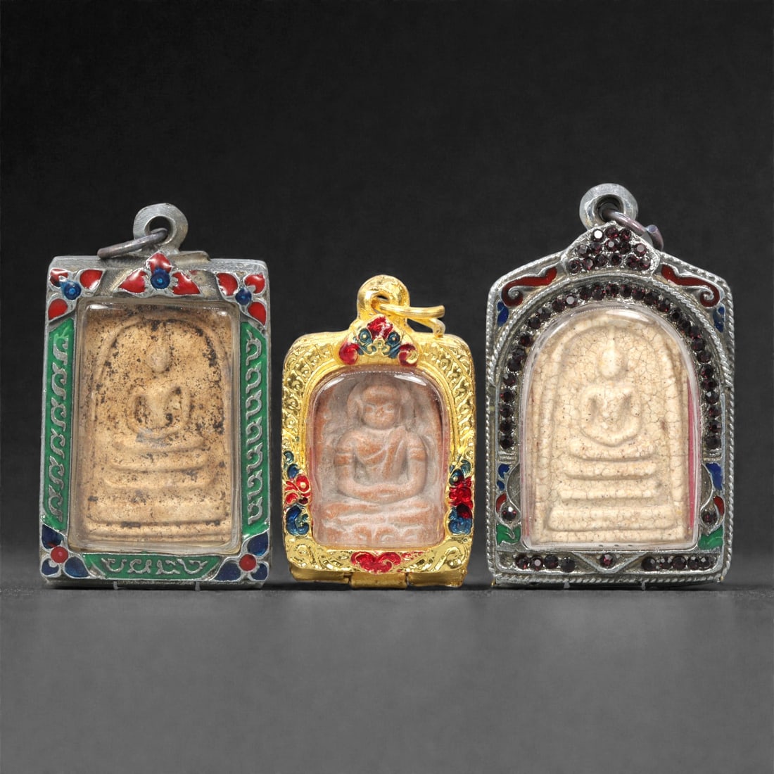 A Group of Thai Clay and Composite Buddhist Amulets, 20th Century, 16ZG: Comprising three molded Buddhist amulets formed from pale buff and light brown clay compositions, each depicting a seated Buddha in meditation posture upon a stepped base. The figures are rendered in