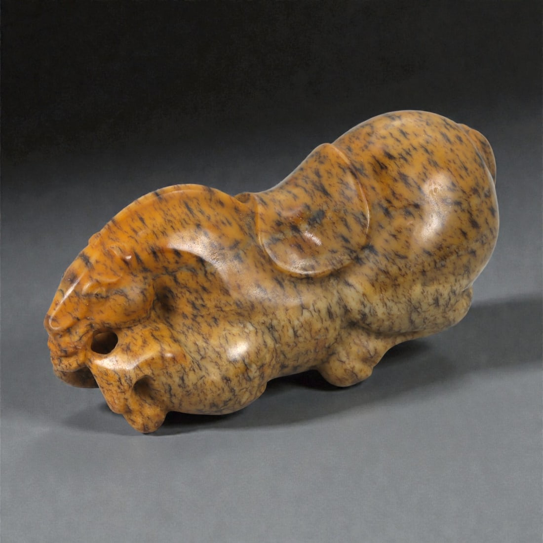A Chinese Hardstone Recumbent Horse Figure, 20th Century, 84YA: Carved from mottled brown hardstone with dark veining and natural tonal variation, the figure is modeled in the round as a recumbent horse with legs folded beneath the body. The head is rendered with