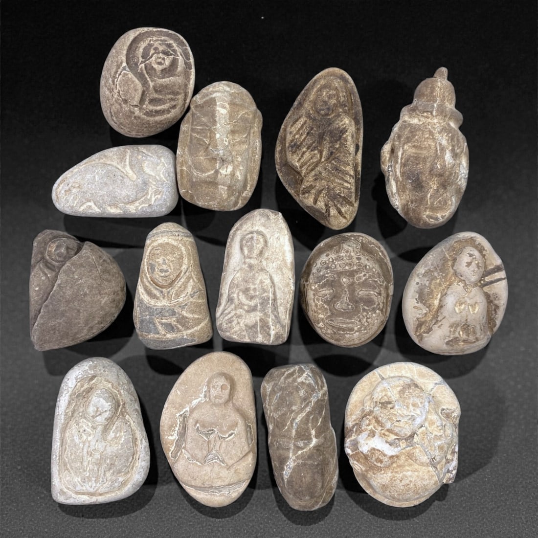 A Group of Japanese Stone Buddhist Figures, Edo Period, 93Z: Carved from light to dark-toned stone with natural inclusions, veining, and areas of surface wear, the group comprises fourteen small Buddhist devotional figures of rounded and irregular pebble-like f